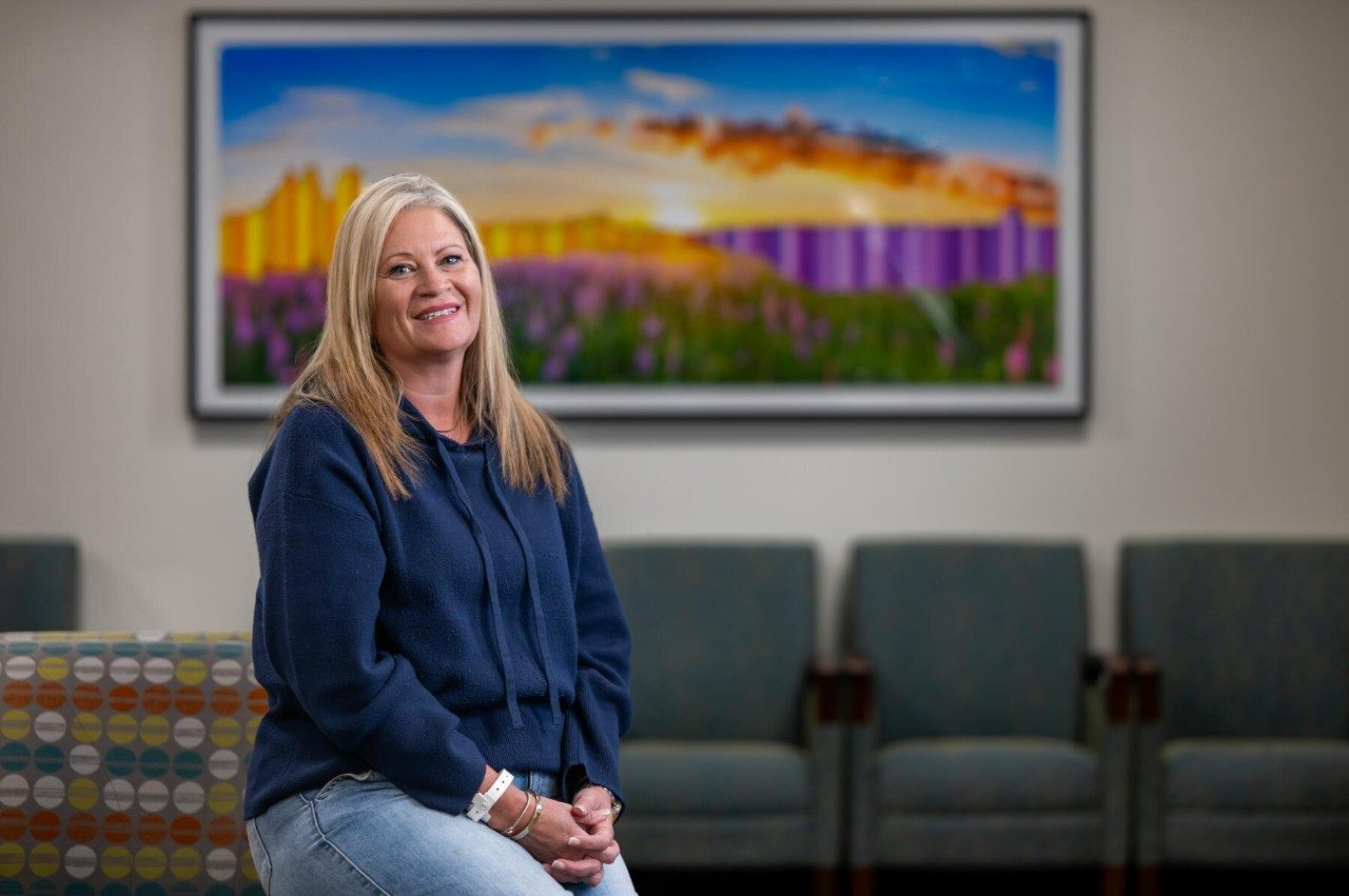 Woman with blond hair wearing a blue sweatshirt sits in a clinic waiting room