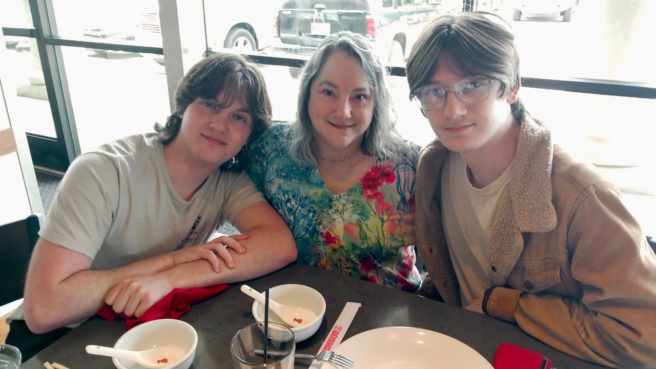 Woman sits at a table with two young adult males