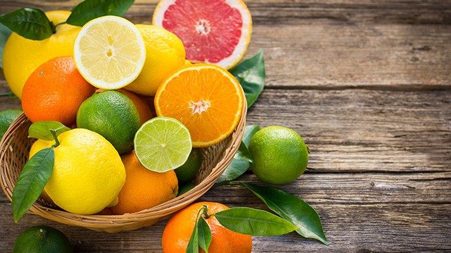 Bowl on rustic wooden table, overflowing with citrus fruit