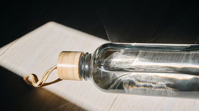 A reusable glass water bottle with a bamboo cap.