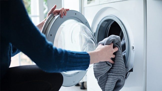 Person crouches in front of a laundry machine to load a towel.