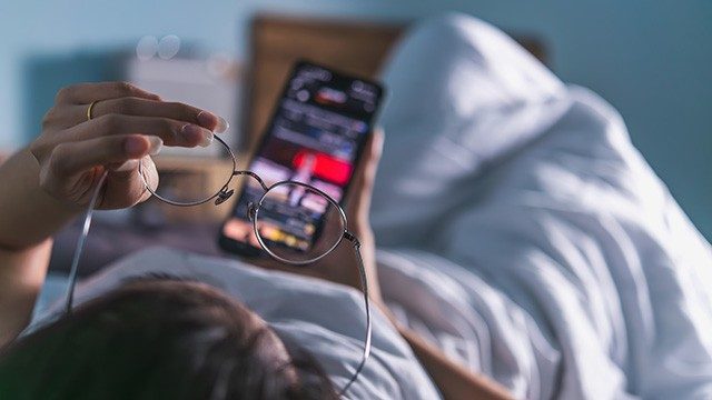 Headboard view of  unidentified person looking at phone in bed