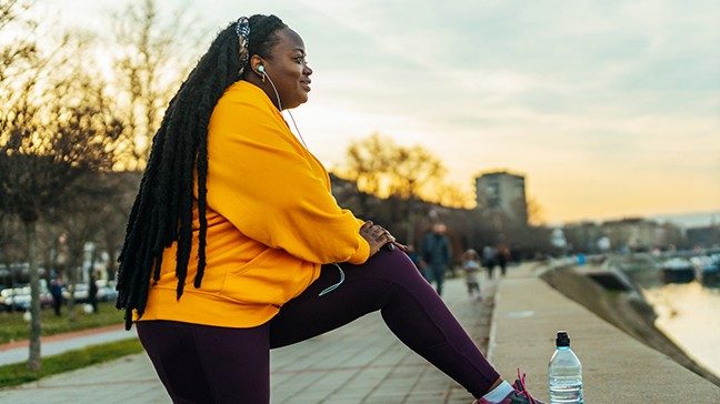 Black woman stretches her leg outside before a workout