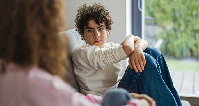 Skeptical teenage boy eyes unidentified mom in living room