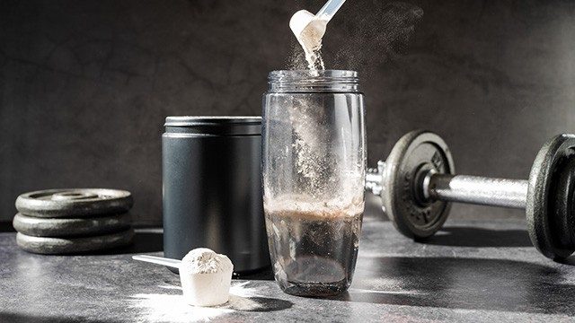 creatine powder being poured into a shaker bottle next to a barbell