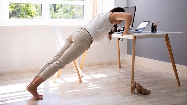 Unidentified woman doing a pushup by leaning against her computer desk