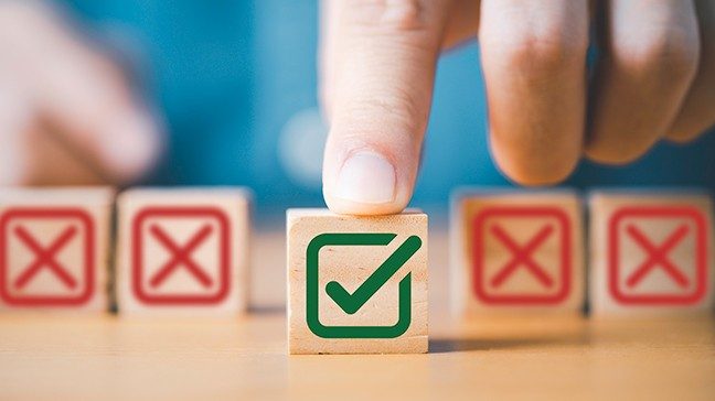 Small wooden block with green checkmark on it set apart from four others with red Xes 