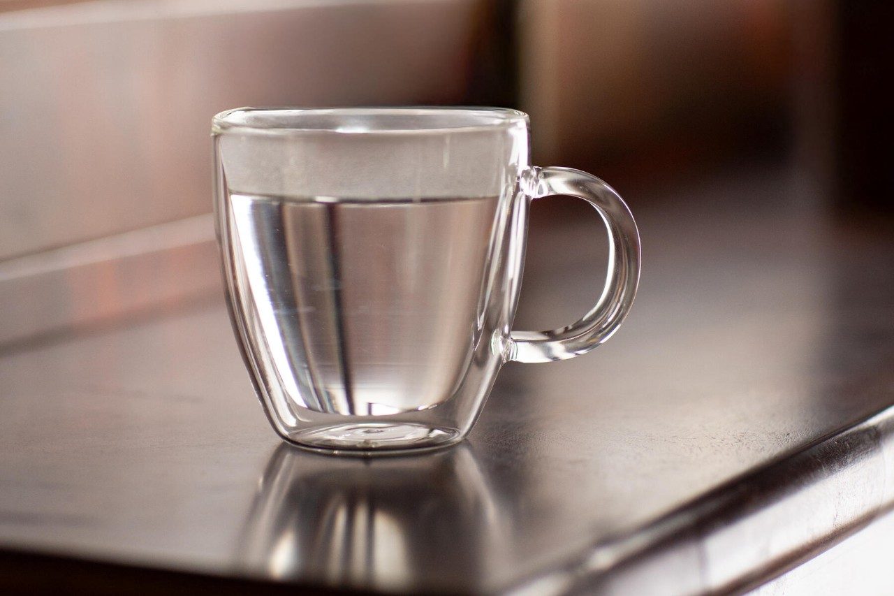 clear mug of hot water sitting on a desk, benefits of drinking hot water