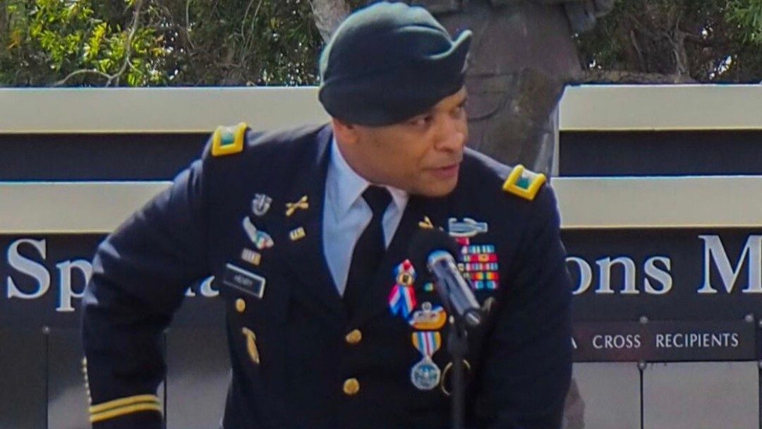 Man standing at a podium in U.S. military uniform wearing decorations and awards