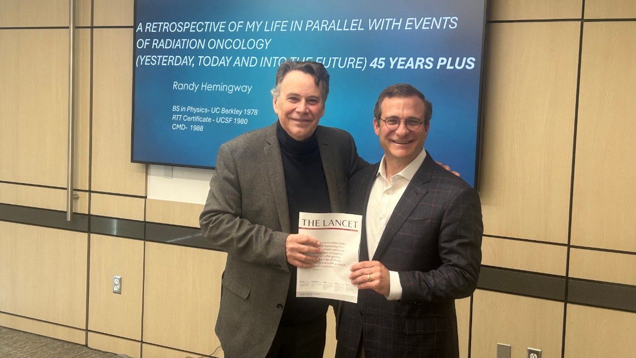 Two men stand together in a classroom holding a journal report