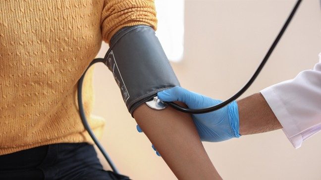 A medical professional wearing gloves and a white jacket checks a woman's blood pressure