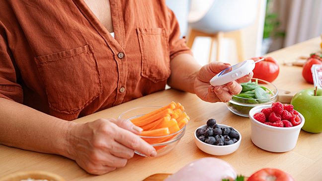 Woman reads a glucometer with bowls of healthy foods around her.