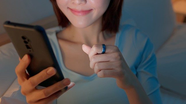 Woman wearing a smart ring while checking related data on her phone, wearable health monitoring devices