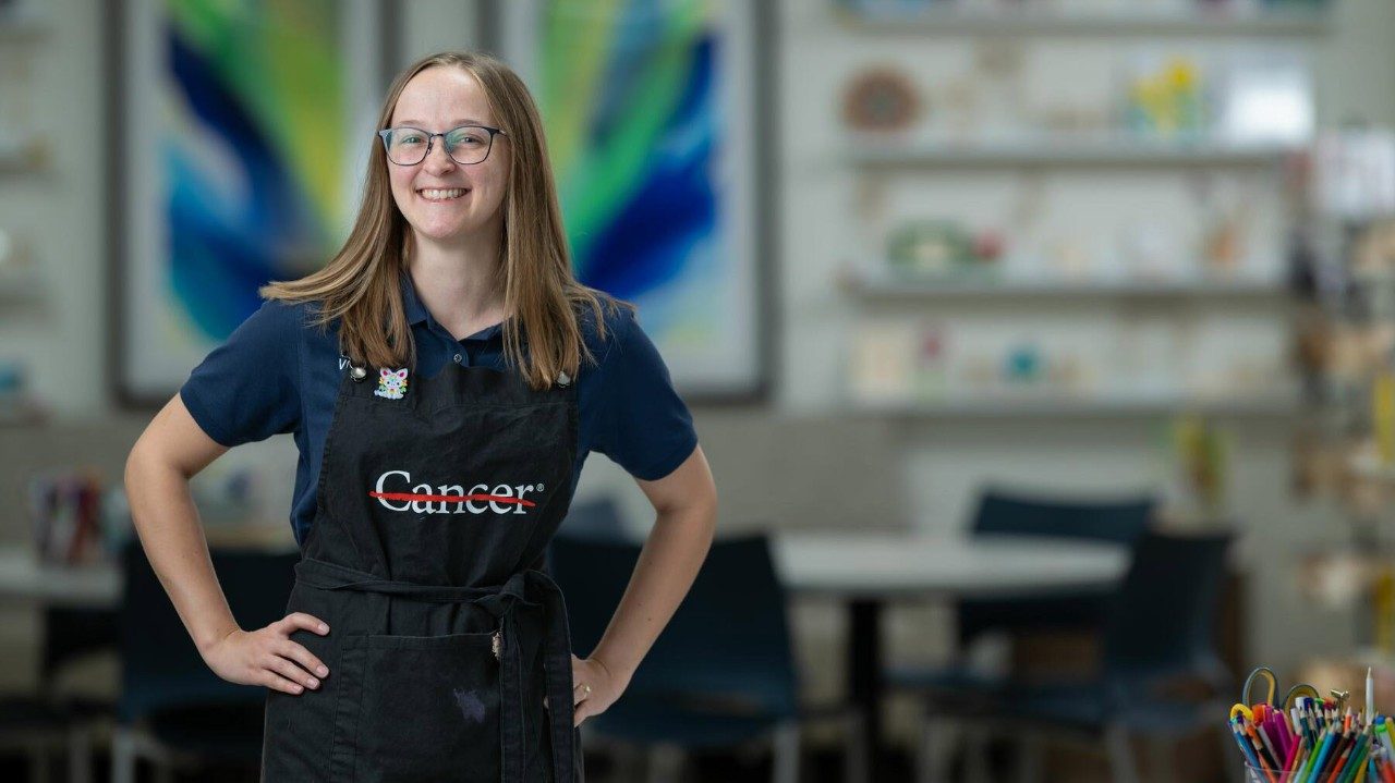 Young woman wears an artist apron with the word cancer on the front and a red line strikethrough