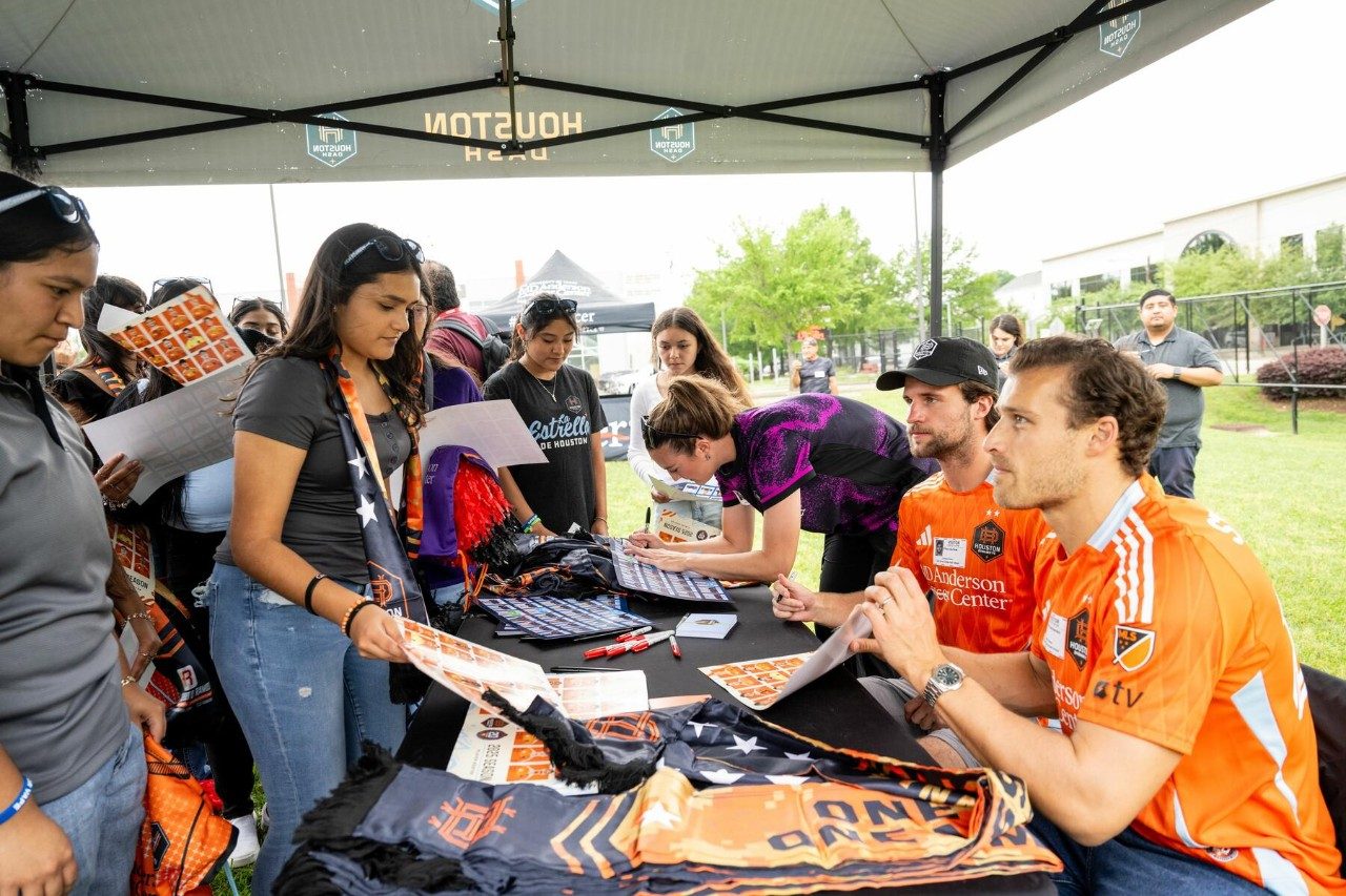 Houston Dynamo FC and Houston Dash players sit at a table signing autographcs for students at Kick Tobacco and Vaping Day