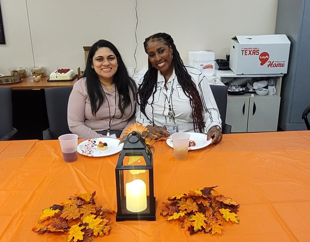 two people posing for a photo while seated at a table with plates containing desserts in front of them