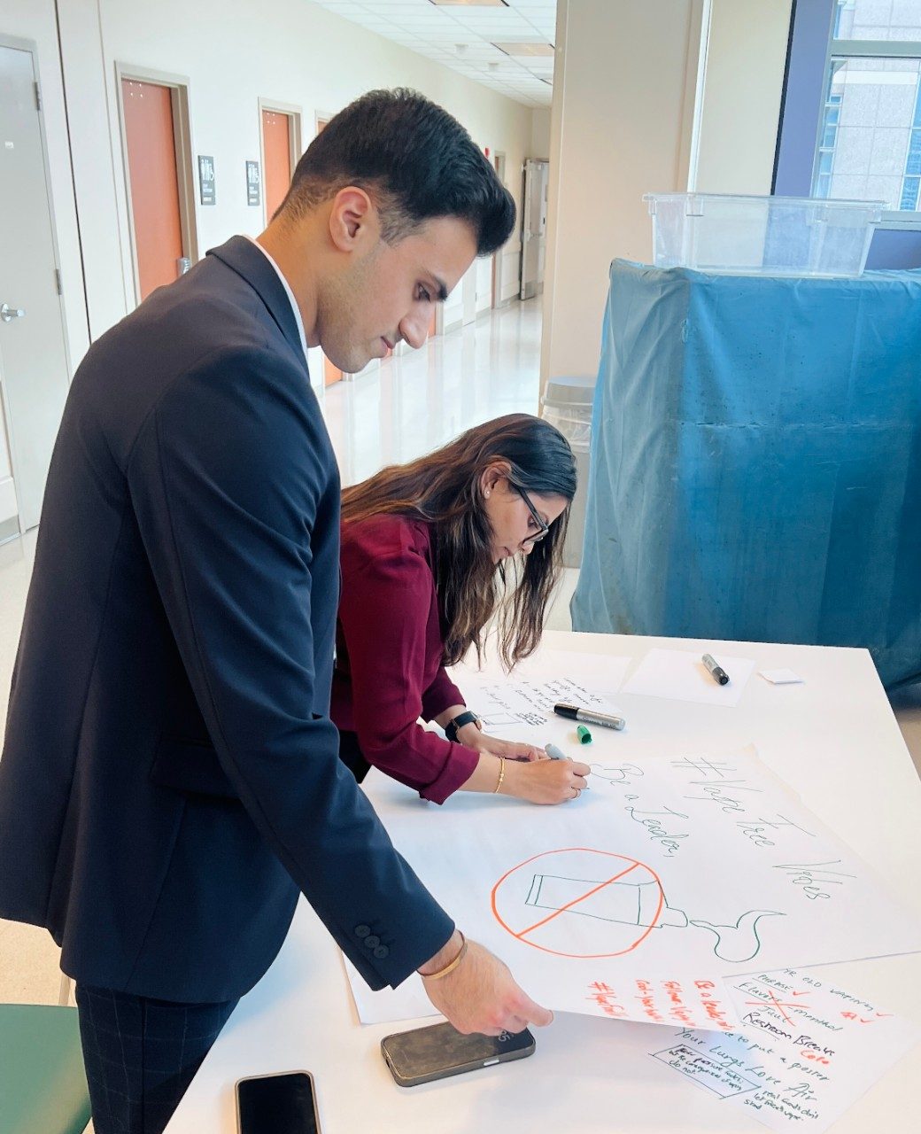two people writing on a poster that is placed on a table