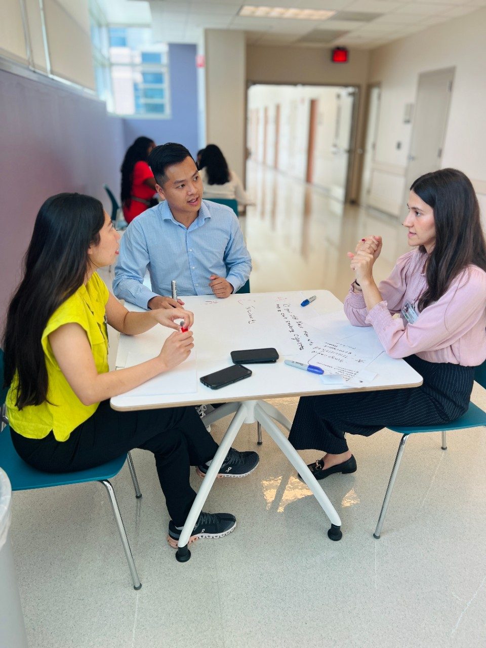 three people sitting at a table working on a poster