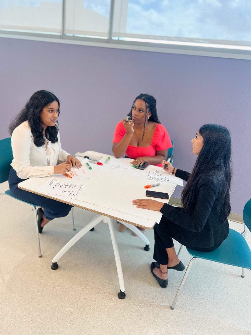 three people sitting at a table working on a poster