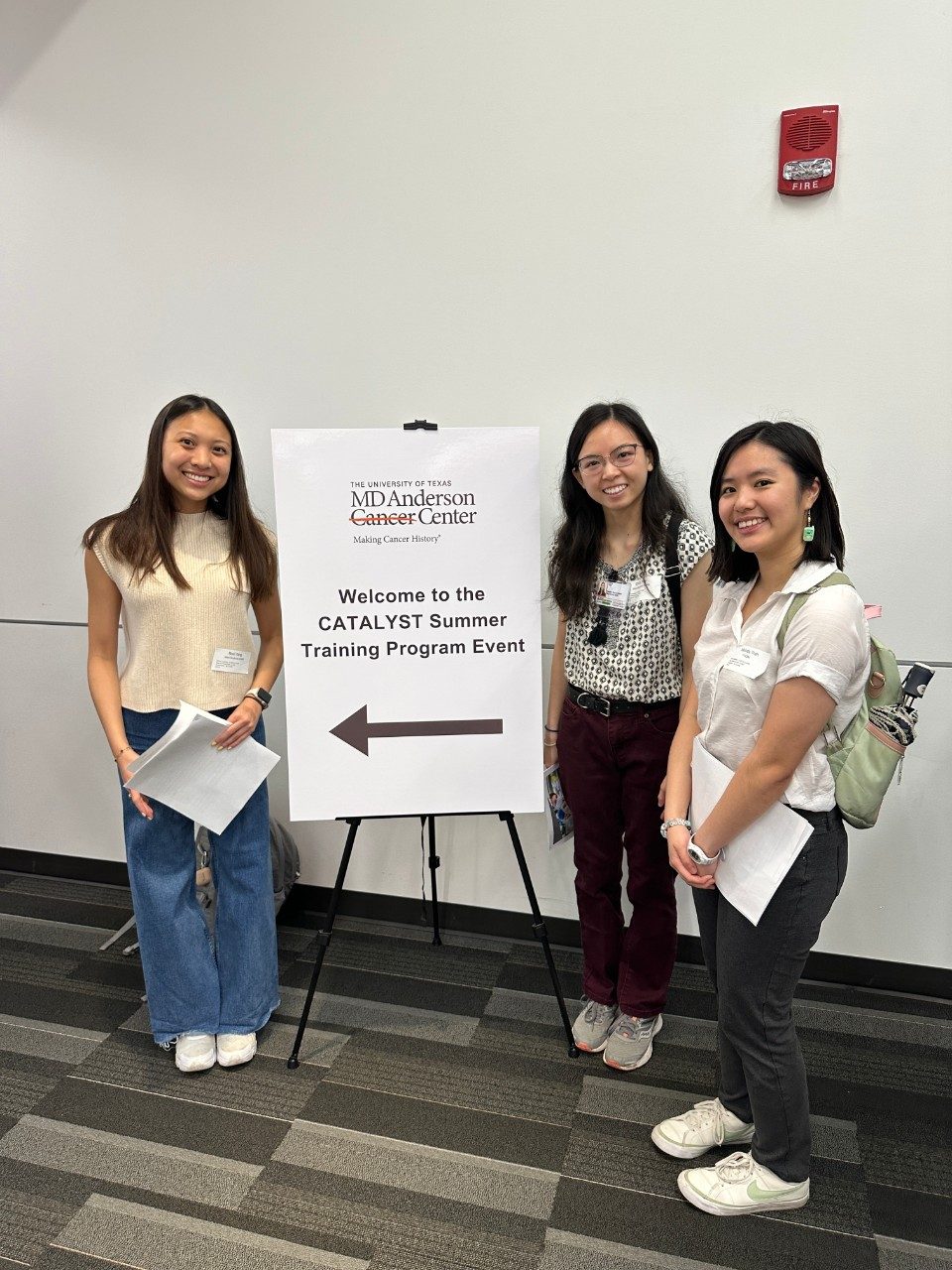 one person standing to the left of a CATALYST Training Program welcome sign, two people are standing to the right of a sign