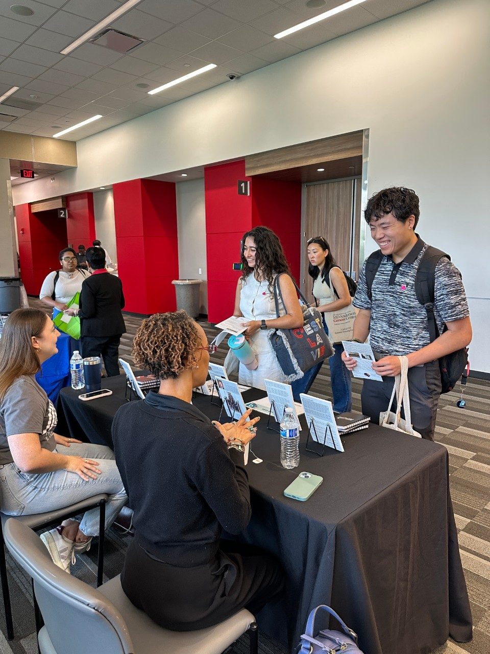 A group of CATALYST Summer Training Program students talking to a person sitting at a table during a resource fair
