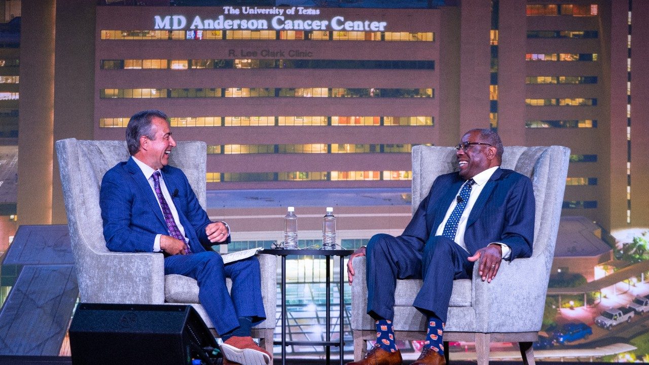 Todd Kalas and Dusty Baker sit in high-back chairs on stage as they talk and smile.