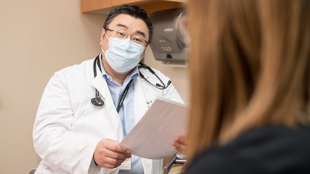 Timothy Yap, M.D., speaks with a patient while wearing a mask