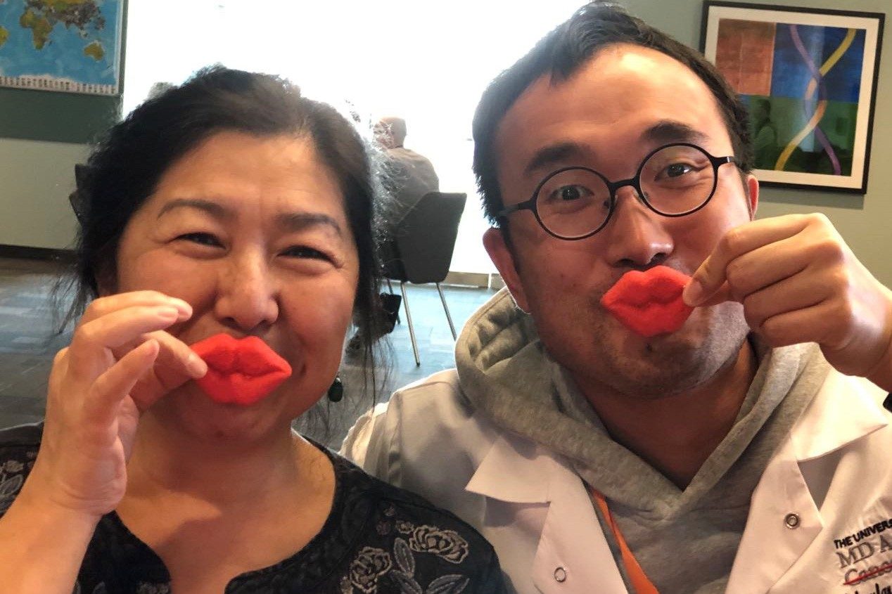 Two people hold red lips in front of their lips