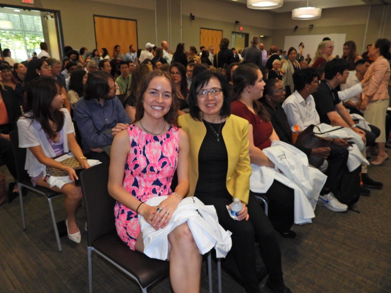 Two people pose in a seated crowd indoors
