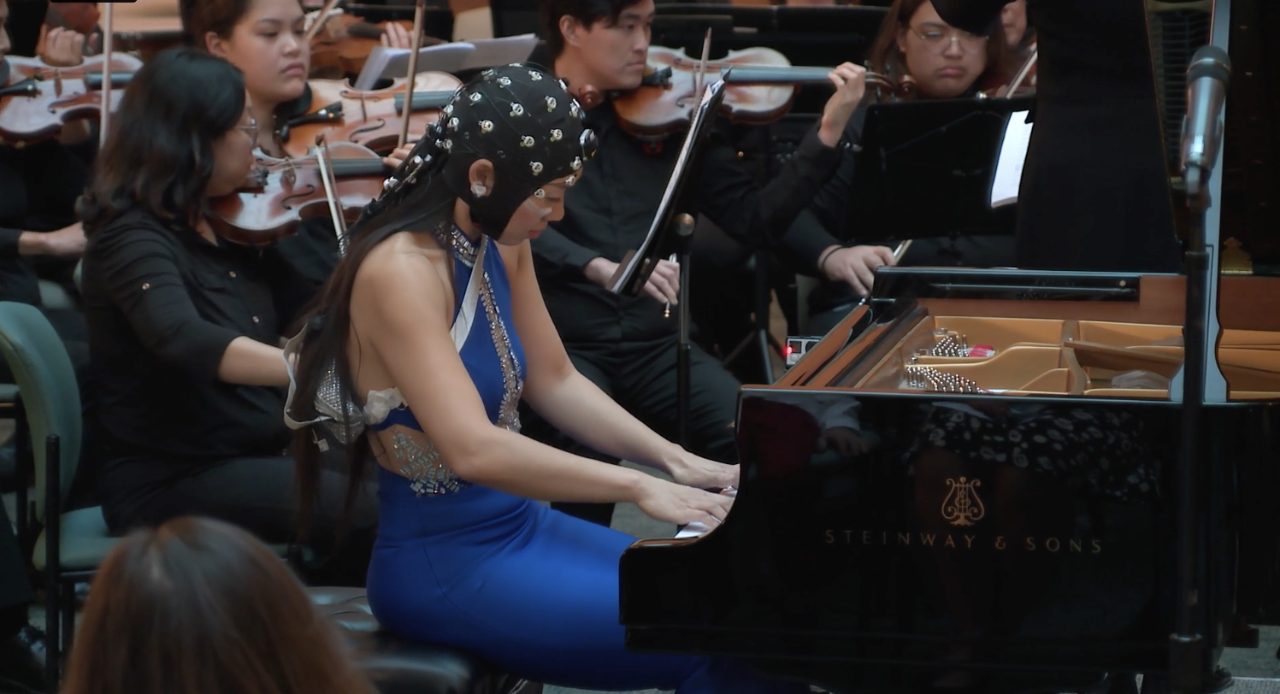 Mei Rui, DMA, playing Rhapsody in Blue and wearing a helmet measuring brainwaves