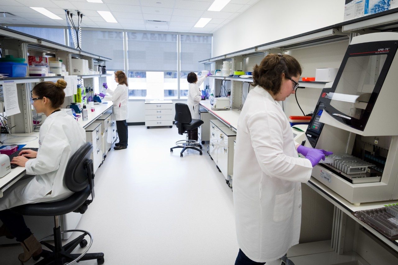 Four people in white coats work in a lab