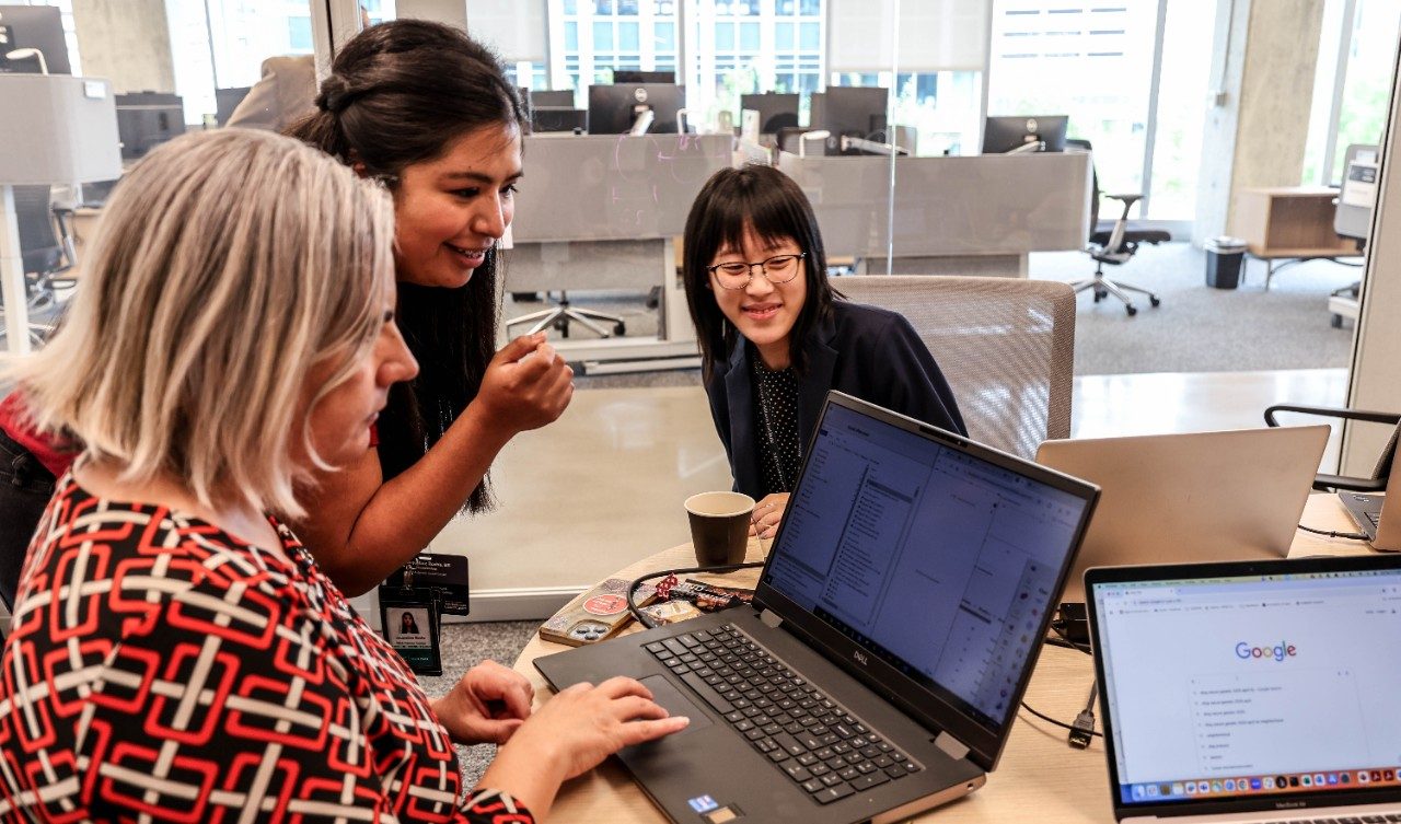 Three people look at a laptop screen