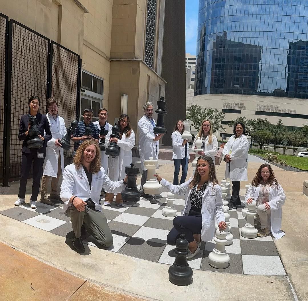 Group of people in white lab coat posed with life-sized chess board and pieces