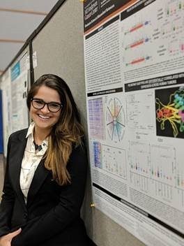 Woman in suit and glasses posing next to poster