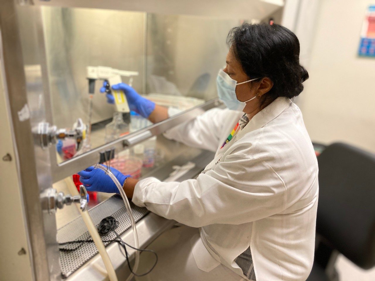 Woman in lab coat and blue gloves working under a hood in a lab