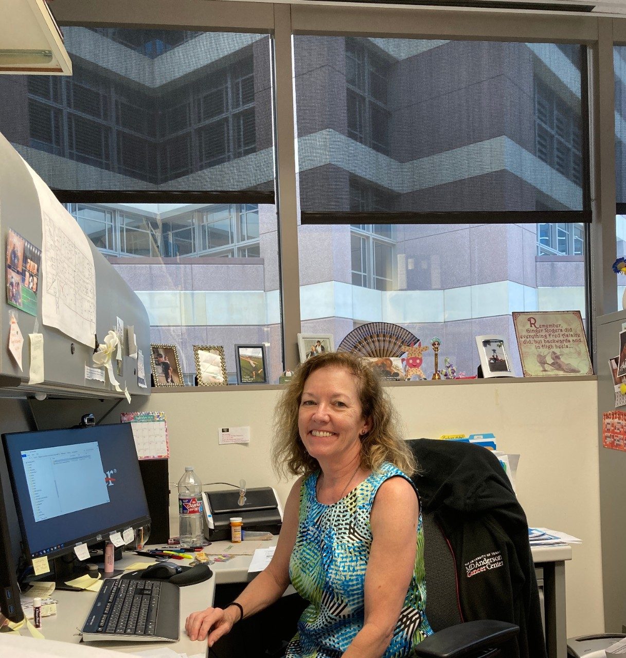 Woman posed smiling in front of a computer in a cubicle