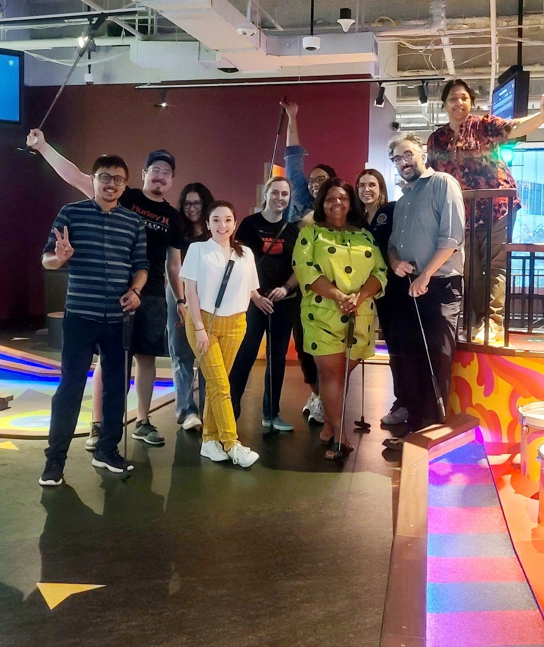 Group of people posing at indoor mini golf, holding golf clubs