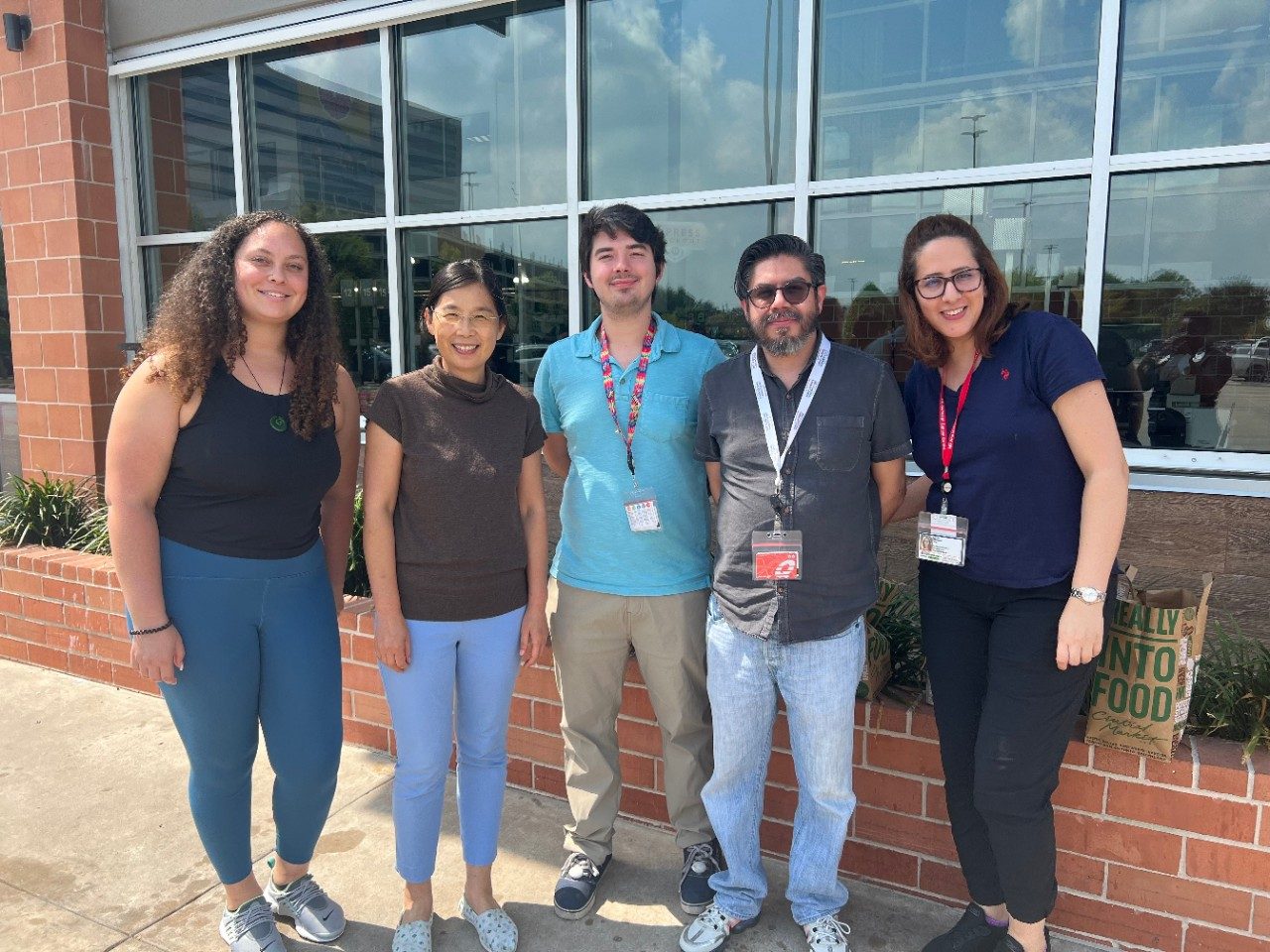 Five people lined up, posing for a photo outside of an MD Anderson building