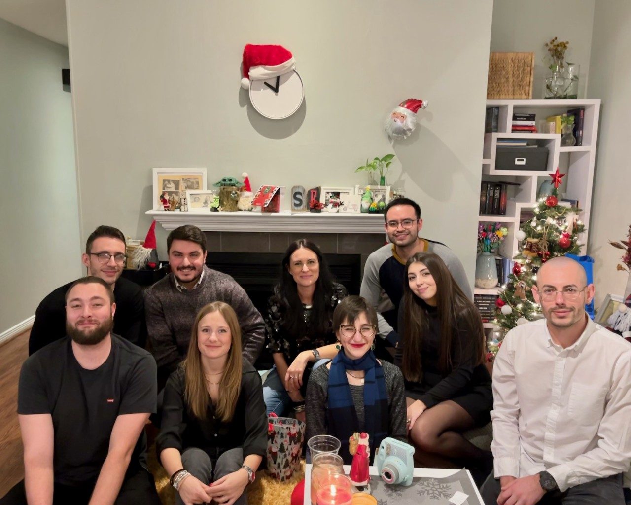 9 lab members posing in front of a fireplace with a Santa-hat-adorned clock