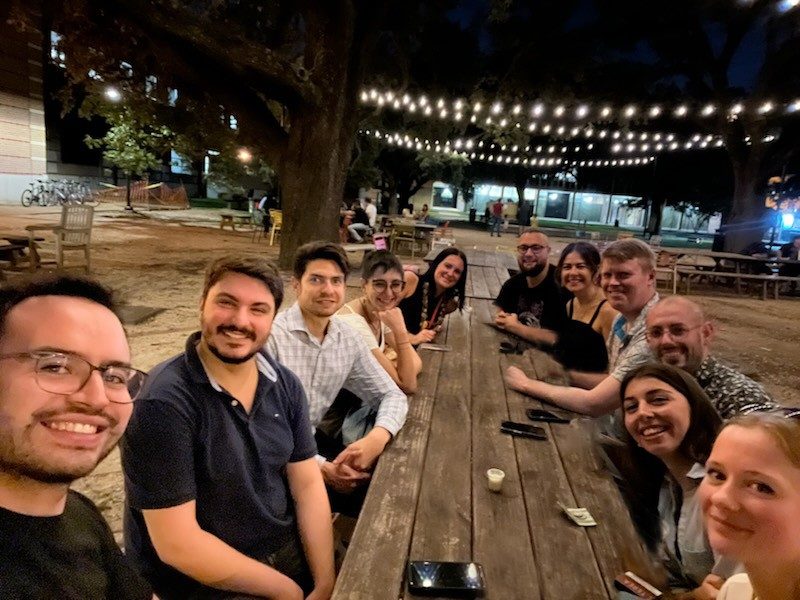 11 people around a long picnic table outside at night
