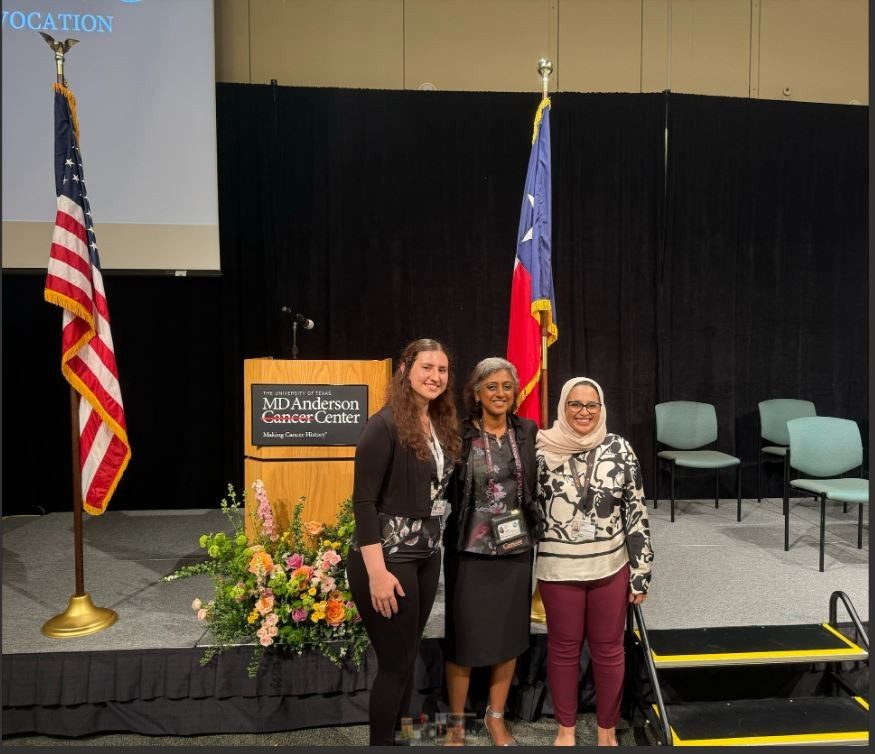 3 adults standing infront podium posing for picture