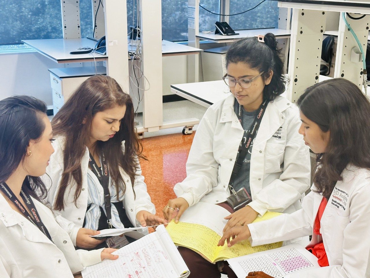 Four women seated in a circle in the lab, comparing notes