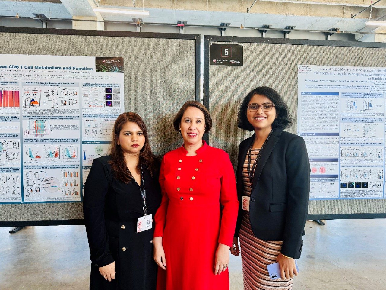 Three women pose in front of poster boards at a conference