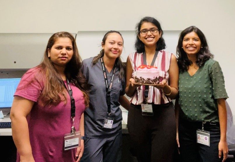 Four women pose for the camera; one is holding a cake