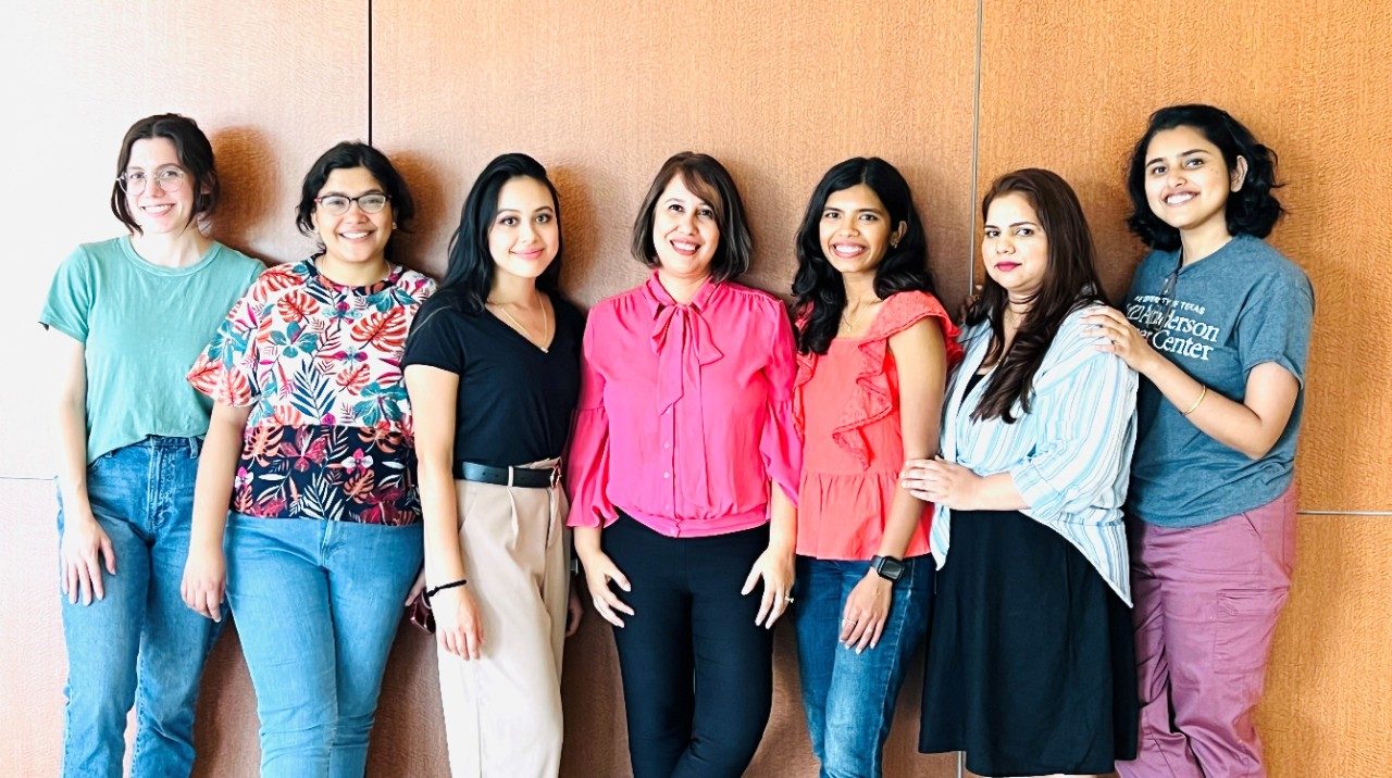 Seven lab members stand in front a wall, posing