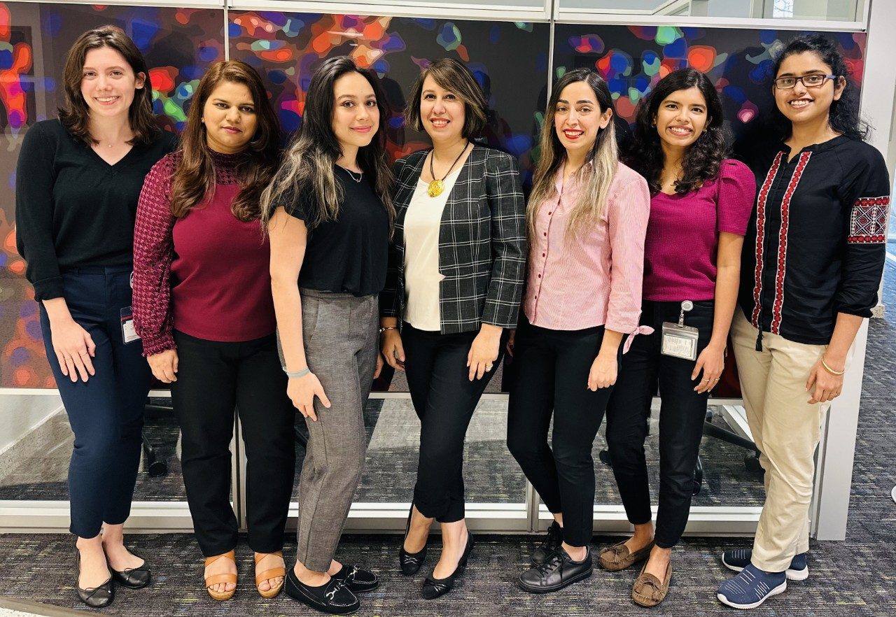 Seven lab members pose in front of a blown up microscope image on the wall