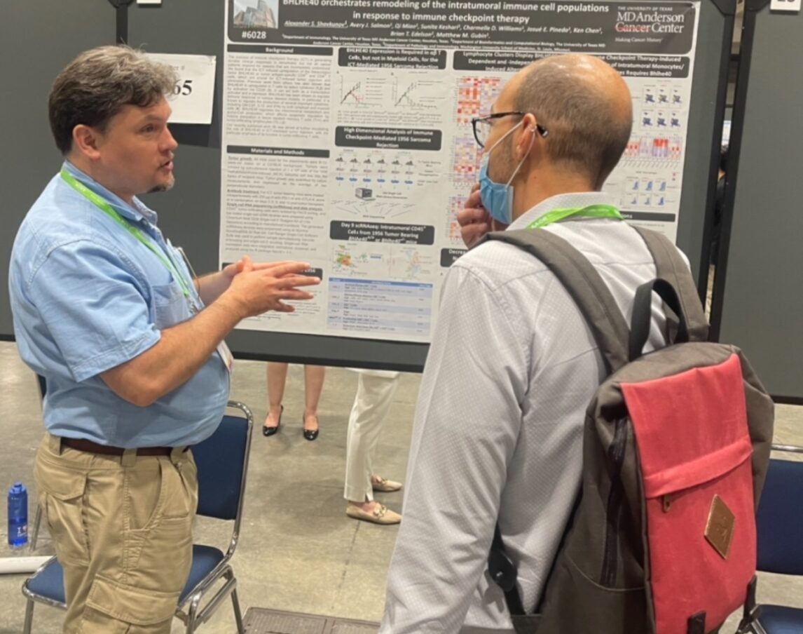 Two people standing in front of a poster with one gesticulating while explaining