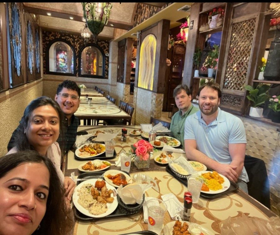 Five lab member smile for a selfie around a restaurant table loaded with food