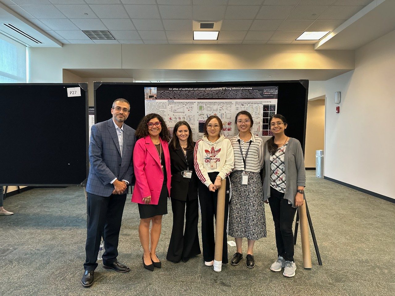 Dr. Kadara and five lab members lined up in front of a poster