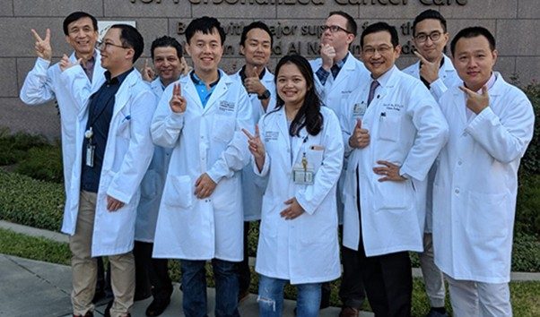 Members of the Lin Laboratory pose for a photo wearing white lab coats outside of the Zayed building